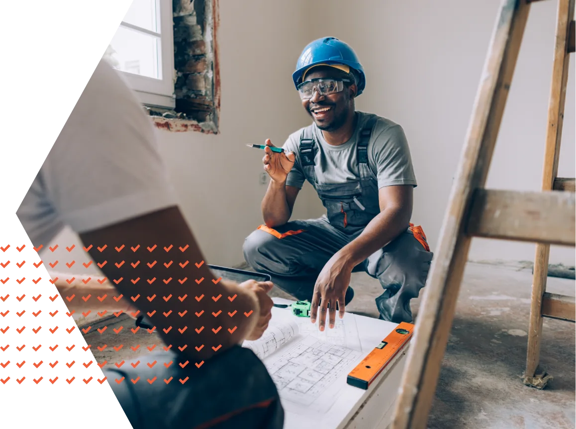 Construction worker on job site squatting next to blueprint smiling